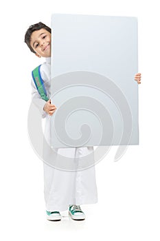 Arab school boy raising a big white board with both hands, wearing white traditional Saudi Thobe and sneakers, raising his hands photo