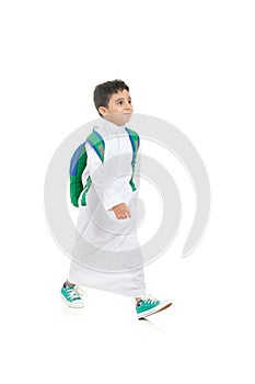 Arab school boy smiling and walking, wearing white traditional Saudi Thobe, back pack and sneakers, raising his hands on white photo