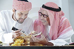 Arab senior and young man smiling and holding Brix Refractometer and glass plate contain piece of date palm for test sweetness