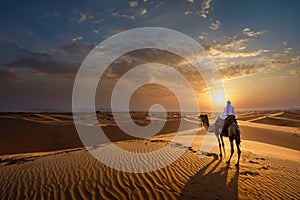 An Arab sits on a camel and looks at the sunrise. An Arab herdsman sits in the desert looking to the west