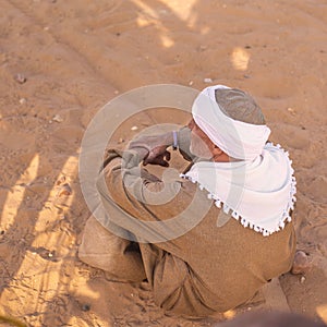 Arab traditional dressed man siting in desert and looking towards Pyramids in Cairo Egypt