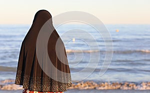 arab woman with black veil to cover her head by the sea awaits t