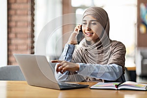 Arab woman in headscarf having conversation on phone at cafe