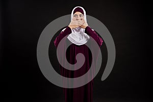 Arab woman in hijab covers mouth with hands.