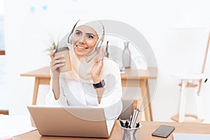 An Arab woman in hijab listens to music on headphones.