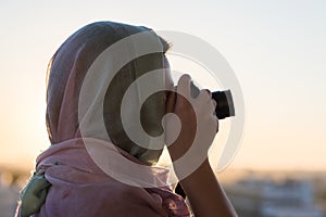 Arab Woman Photographer in a scarf taking picture using Camera on the sunset background.