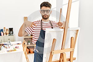 Arab young man at art studio pointing down looking sad and upset, indicating direction with fingers, unhappy and depressed