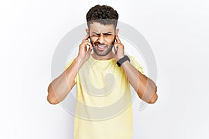 Arab young man standing over isolated background covering ears with fingers with annoyed expression for the noise of loud music