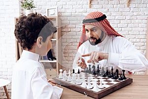 Arabian bearded father and little son play chess.