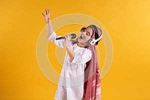 Arabian boy in keffiyeh with microphone sings karaoke.