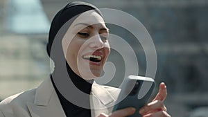 Arabian businesswoman dressed in hijab using smartphone, walking in Business Quartal, having good news on cellphone