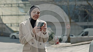 Arabian businesswoman dressed in hijab using smartphone, walking in Business Quartal, having good news on cellphone