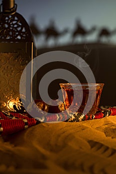 Arabian carpet with tea cups, lantern, dates, camels in a desert sand dunes