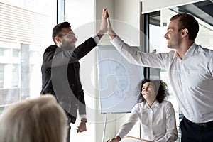 Arabian Caucasian corporate buddies greeting each other giving high five