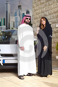 Arabian couple against their car posing at home with cityscape behind