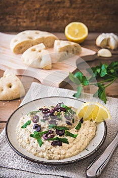 Arabian cuisine: Baba Ganoush with black olives and minced parsley and flatbread on a rustic wooden table