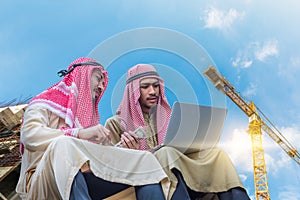 The arabian engineer talking about business job and using laptop with construction site and crane background