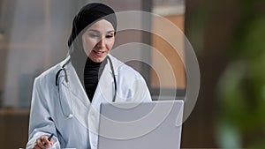 Arabian female therapist doctor wear hijab white coat calling distant patient on laptop talking with client in remote