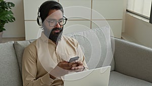 Arabian Indian businessman man multitasking working with devices at home muslim guy in headphones talk video chat