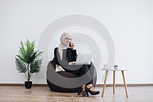 Arabian lady having phone call with computer on laps at work