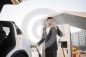 Arabian man drinking coffee while charging car
