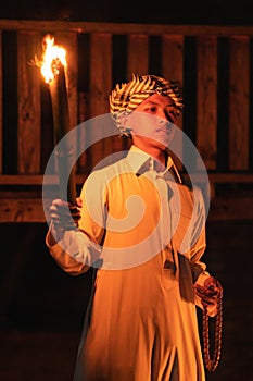 An Arabian man holding a fire torch in the front of a wooden house