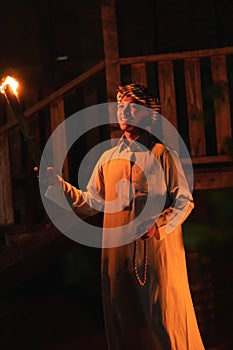 An Arabian man holding a fire torch in the front of a wooden house