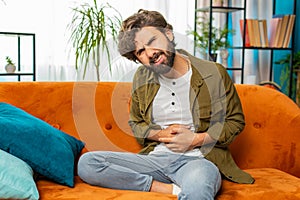 Arabian man sits on sofa feeling sudden strong abdominal stomach ache, gastritis problem, diarrhea