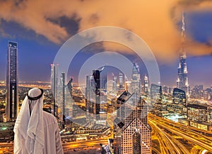 Arabian man watching night cityscape of Dubai with modern futuristic architecture in United Arab Emirates