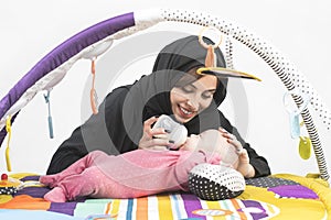 Arabian Mother feeding her baby girl on a play mat .