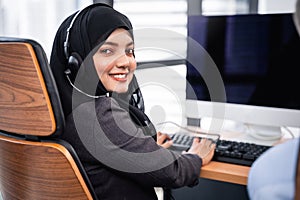 Arabian or Muslim woman works in a call center operator and customer service agent wearing microphone headsets working on computer