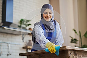 Arabian woman cleaning a kitchen table, using a rag and wearing gloves