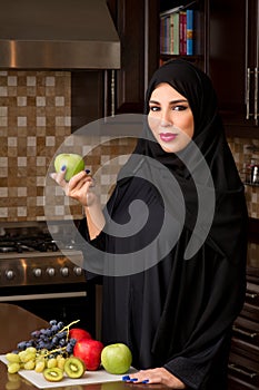 Arabian woman holding an apple in the kitchen