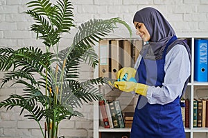 Arabian woman wiping dust off the leaves in the office and smiling