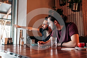 Arabian young men talking in lounge bar. Multiracial friends look at window and point outside