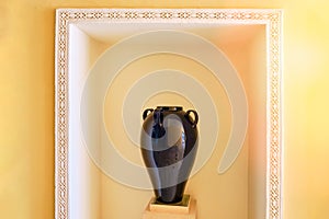 Arabic antique vase on a pedestal as an element of decor in hotel. A large black amphora with two handles in a niche in the yellow