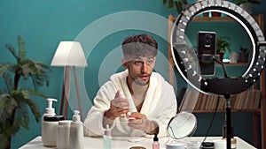 Arabic beauty blogger streaming via phone while doing face care routine, man sitting at desk using cotton pad and tonic