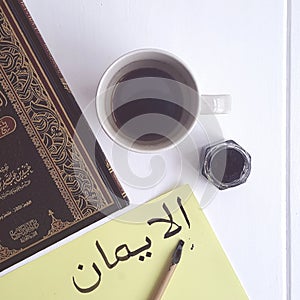 Arabic calligraphy Al Iman - Faith on table with coffee and Islamic book. Photo. photo