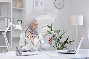 Arabic female doctor in hijab greeting remote client while providing online consultation from private clinic. Medic
