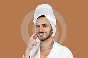 Arabic Guy Applying Cream On Face Moisturizing Skin, Brown Background