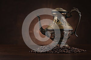 Arabic kettle with coffee beans on brown background