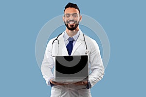 Arabic Male Doctor Showing Laptop Empty Screen Over Blue Background