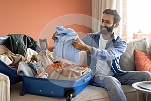 Arabic Man Packing Clothes In Suitcase Preparing Luggage At Home