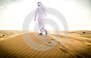 Arabic man with traditional emirates clothes walking in the desert