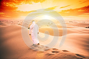 Arabic man with traditional emirates clothes walking in the desert