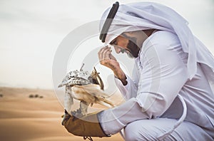 Arabic man with traditional emirates clothes walking in the desert with his falcon bird