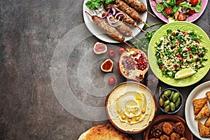 Arabic and Middle Eastern dinner table. Hummus, tabbouleh salad, Fattoush salad, pita, meat kebab, falafel, baklava, pomegranate. photo