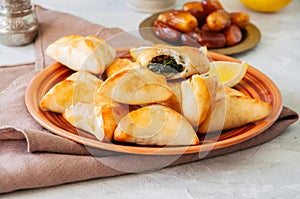 Arabic and middle eastern food concept. Fatayer sabanekh - traditional arabic spinach triangle hand pies dates and tea on a white