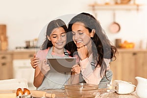 Arabic Mother And Daughter Using Tablet Baking Pastry In Kitchen