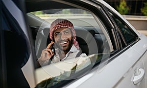 Arabic Muslim businessman looking out car window on mobile phone wearing Keffiyeh